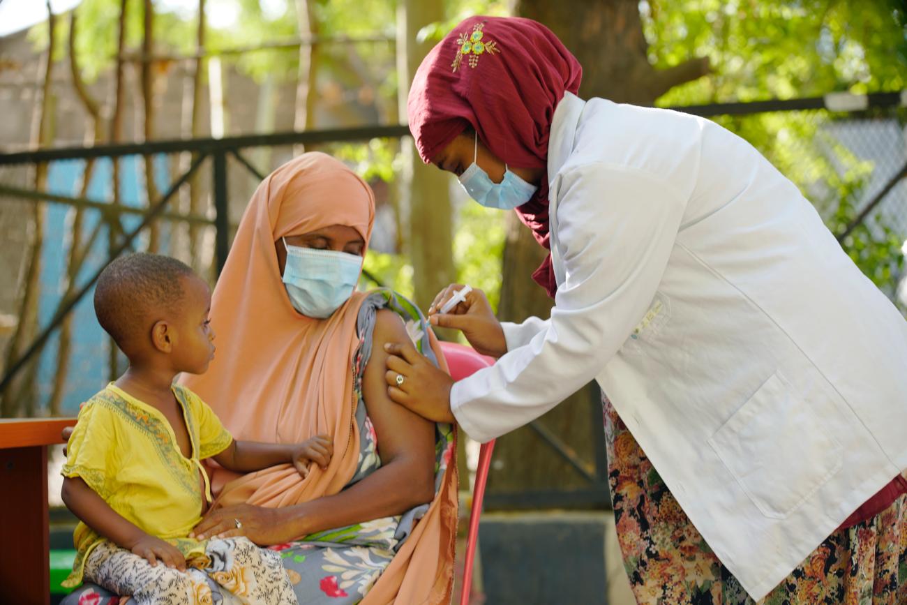 A woman with a child on her lap is vaccinated by a health professional. 