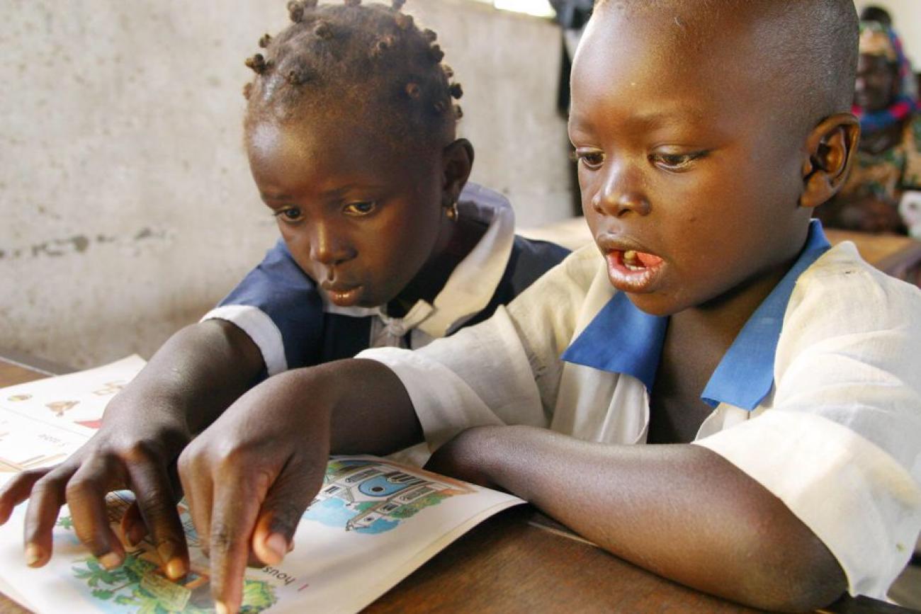 Двое детей в школьной форме читают за партой. 
