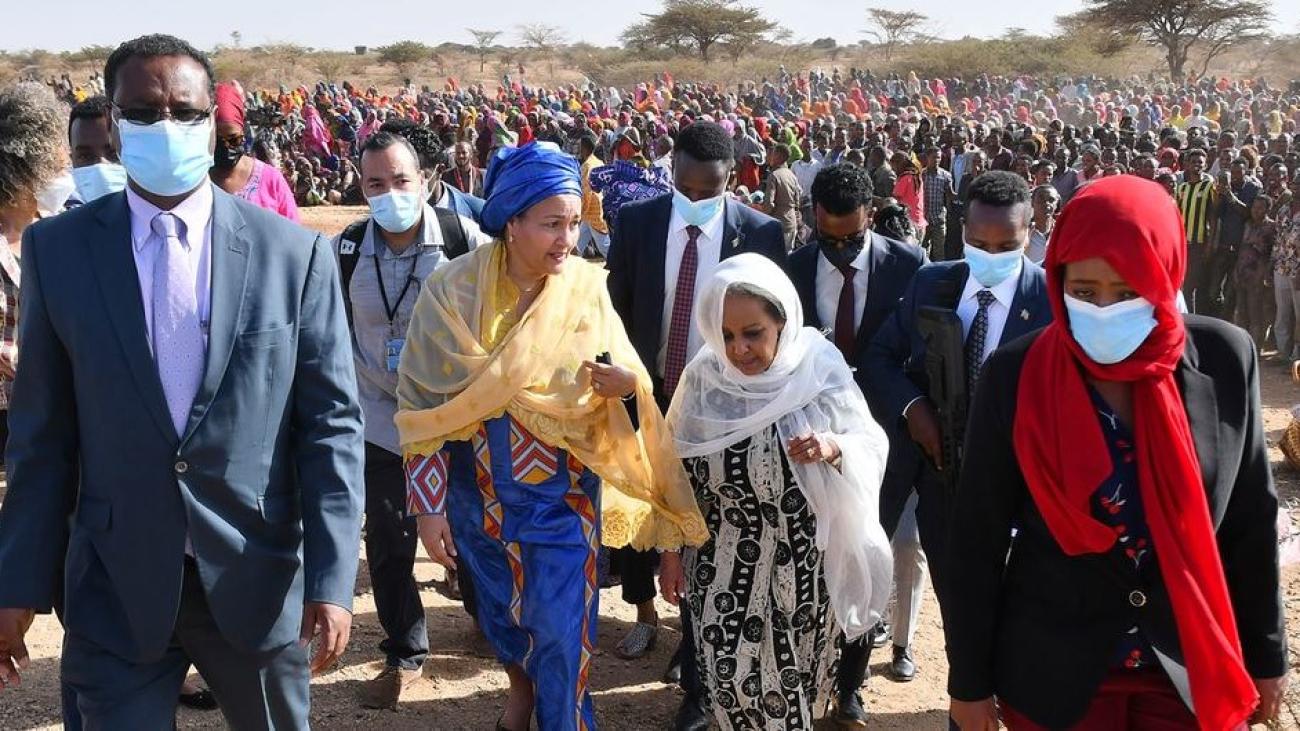 UN Deputy Secretary-General Amina Mohammed and Ethiopian President Sahle-Work Zewde walk surrounded by a crowd in a desert area of Somalia.