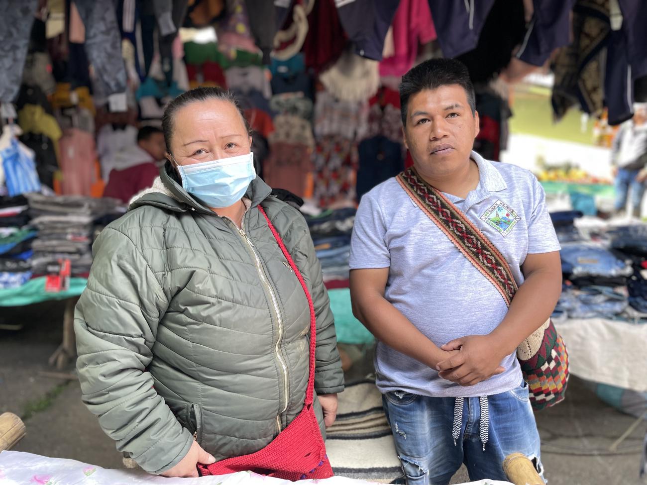 A woman wearing a facemask and a man are standing side by side at a street market. 