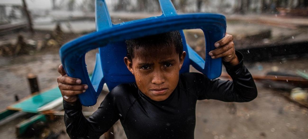 Bajo la lluvia, un niño se cubre con una silla de plástico. En 2020, dos huracanes consecutivos causaron destrucción e inundaciones en toda América Central, dejando a miles de personas sin hogar.