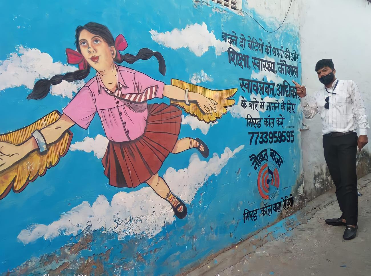 Un homme se tient debout à côté d'une peinture murale montrant une fillette aux cheveux longs et tressés s'envolant dans le ciel en déployant des ailes.