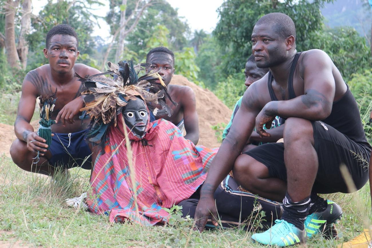 En las afueras de un bosque marfileño, tres jóvenes se agachan en el suelo alrededor de una máscara tradicional. Están a punto de participar en un torneo de "carrera de máscaras" en el condado de Biankouma.