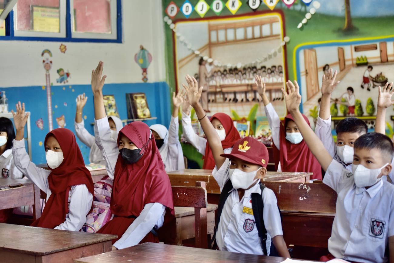 Niños y niñas levantan la mano con entusiasmo en una escuela de Indonesia.