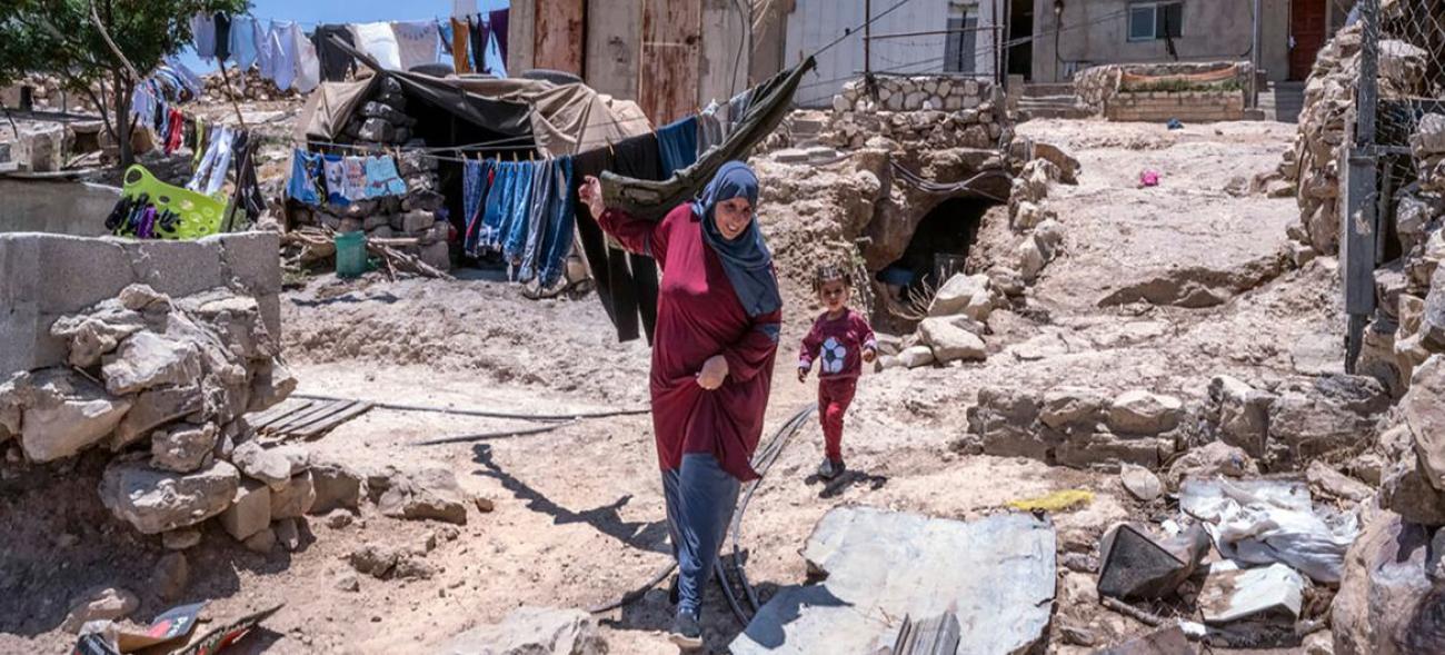 A Kirbet-at-Tabban, dans le sud de la Cisjordanie, une femme voilée suivie par une petite fille se fraye un chemin au milieu d’un terrain vague jonché de pierres et de morceaux de ferraille situé à l’extérieur d’une maison délabrée.