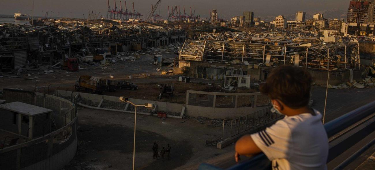 Un jeune garçon regarde le port dévasté de la ville de Beyrouth depuis un balcon.
