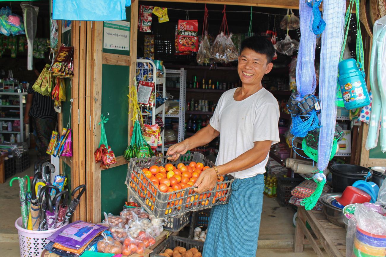 A man holds a basket of oranges, in a market place. 