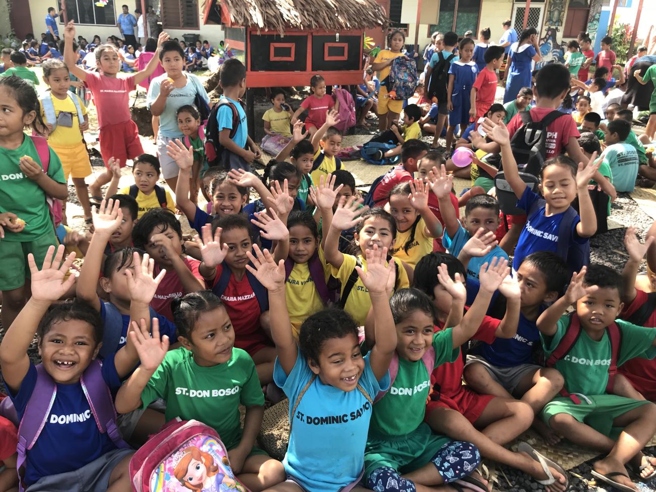 أطفال يرتدون ملابس ملونة يرفعون أيديهم في الهواء.
