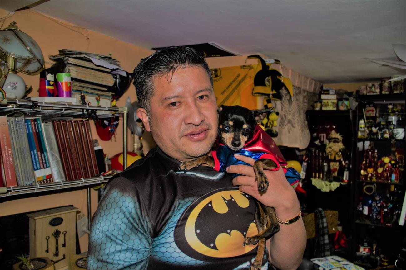 During a remote teaching session, a close-up of the teacher Jorge Villaroel and his dog assistant in a room crowded with books and toys.