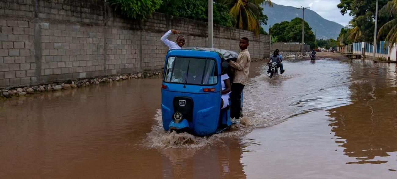 Two boys standing inside a motor vehicle that is stuck in the middle of a flood