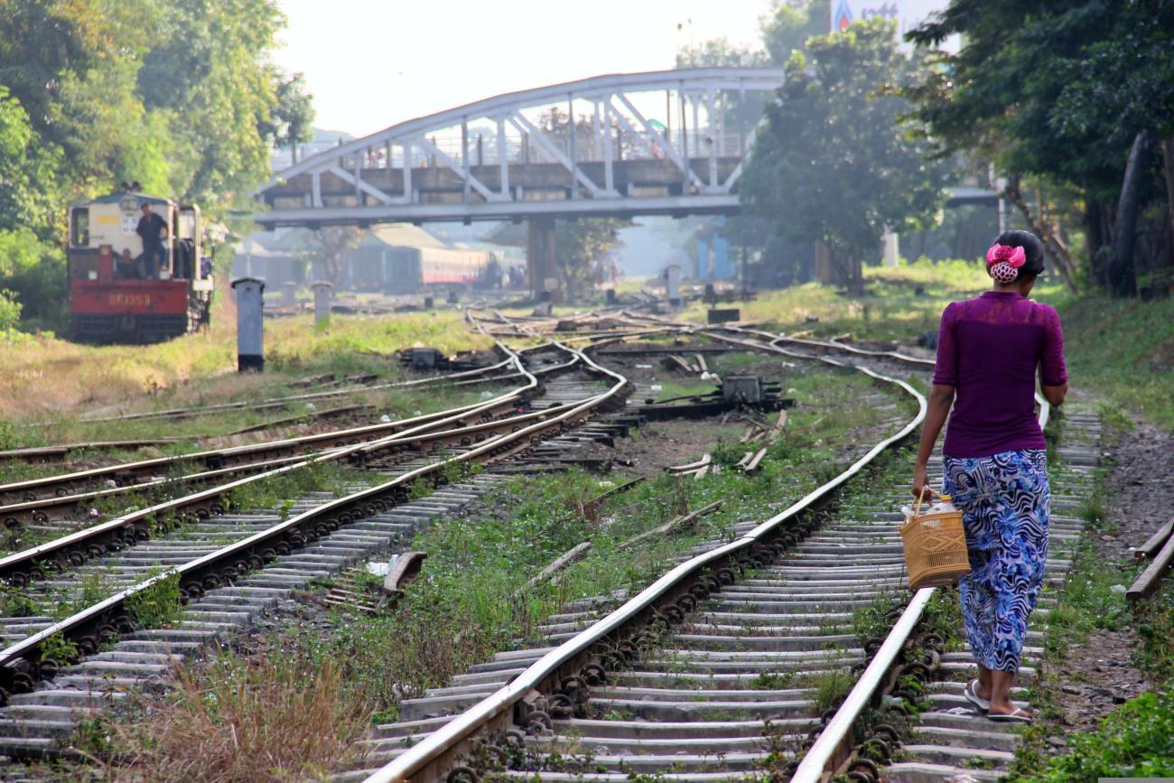 A woman in a purple top walks along a railroad on a sunny day. 