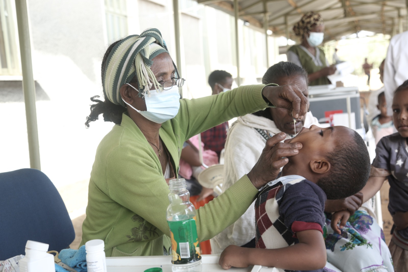 A woman in a green shirt administers an oral vaccine to a boy.