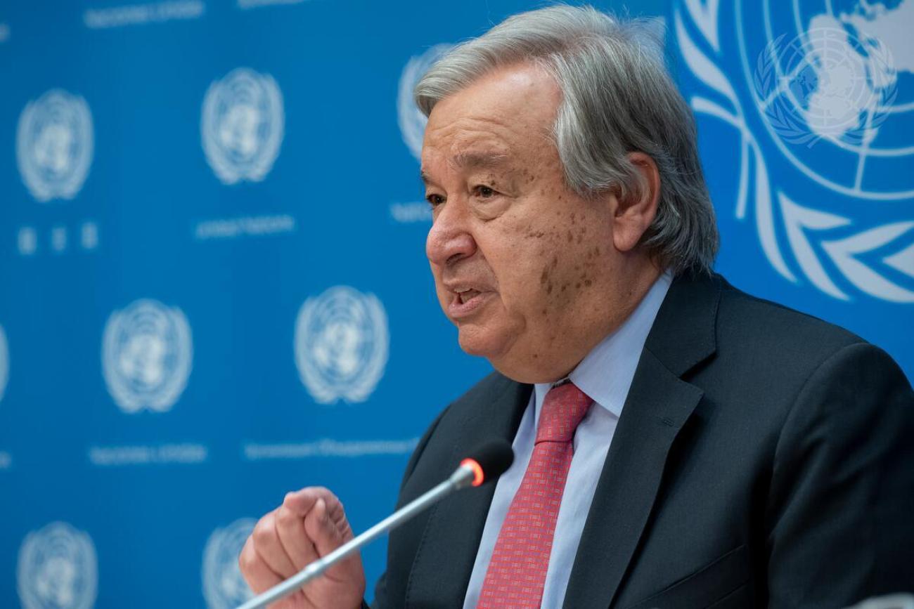 UN Secretary-General Antonio Guterres in a black suit and red tie speaking into a microphone