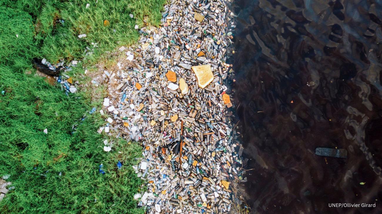 A large track of plastic waste between green land on one side and water on the other side