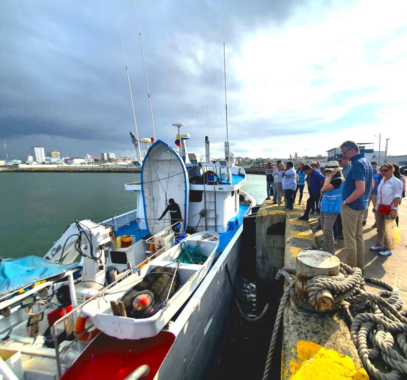 A group of people in blue vests and hats gather around a boat that sits on the water in Manabi, Ecuador