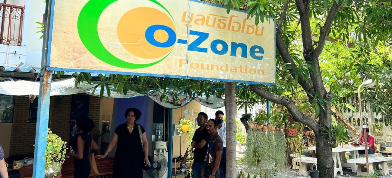A bright yellow billboard saying "Ozone" underneath which a group of people are gathered