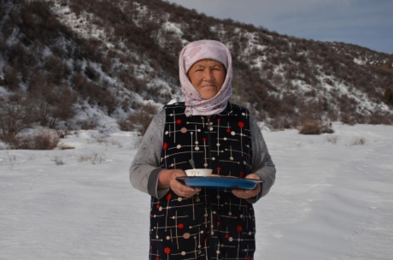 A Kyrgyz woman in a black dress and woollen headscarf holds a piece of ice