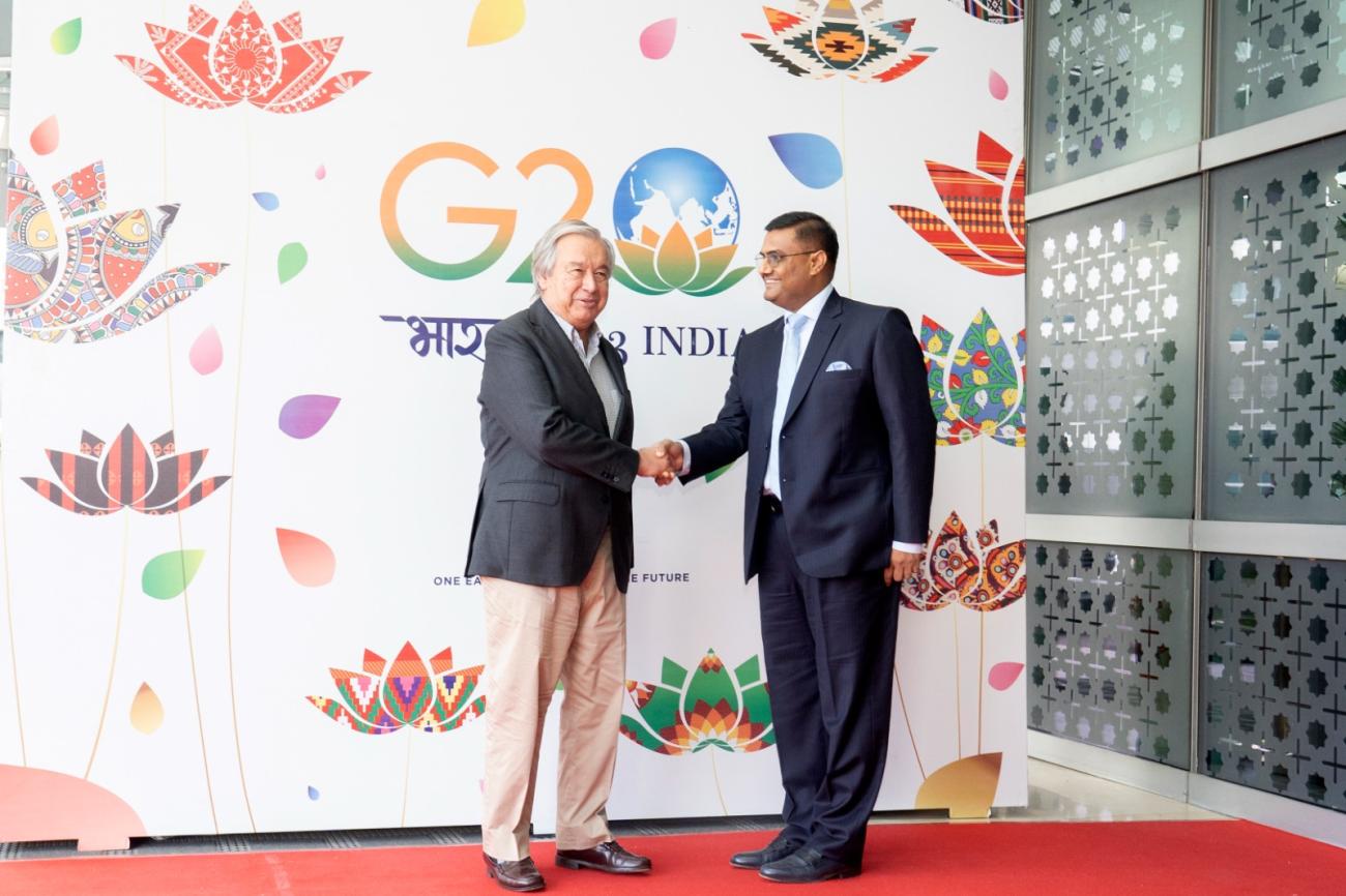 Two men in suits shake hands in India in front of a colourful banner