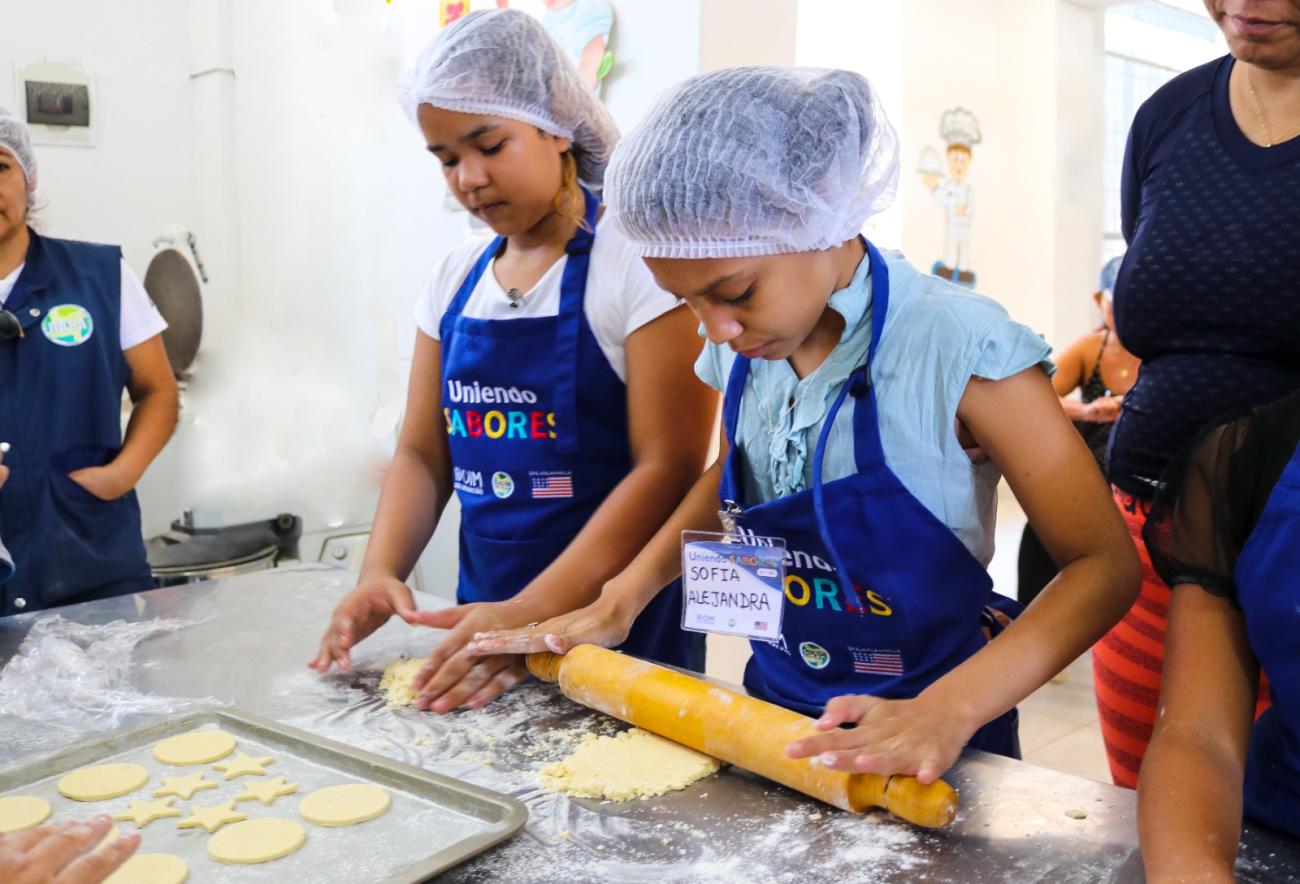 Two children roll a rolling pin on a baking sheet as they participate in a new UN programme