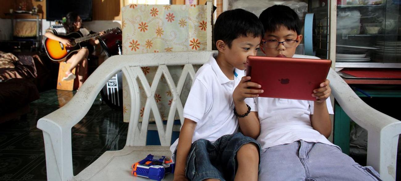 Два мальчика сидят на кресле и смотрят в планшет