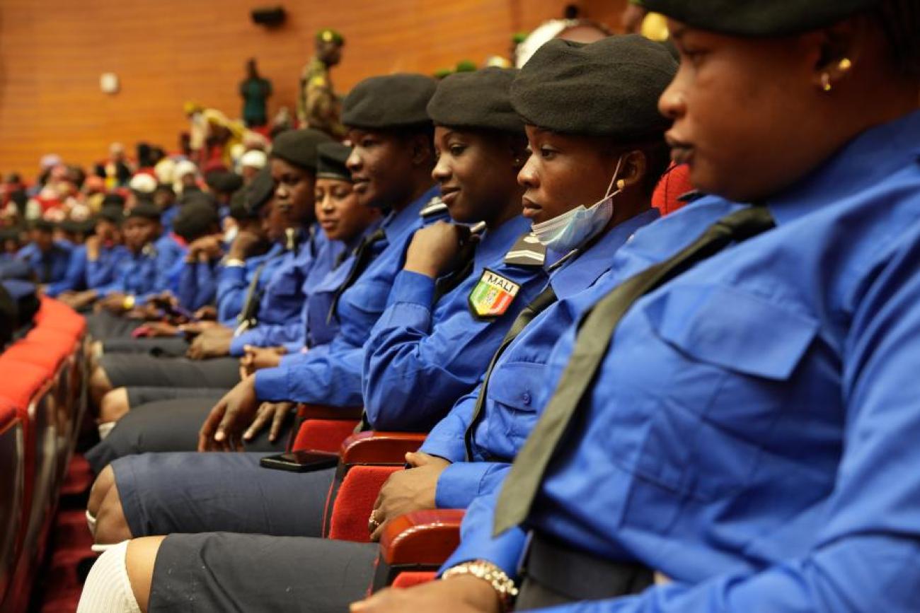 A row of women in blue police style uniforms with black berets, sitting on chairs