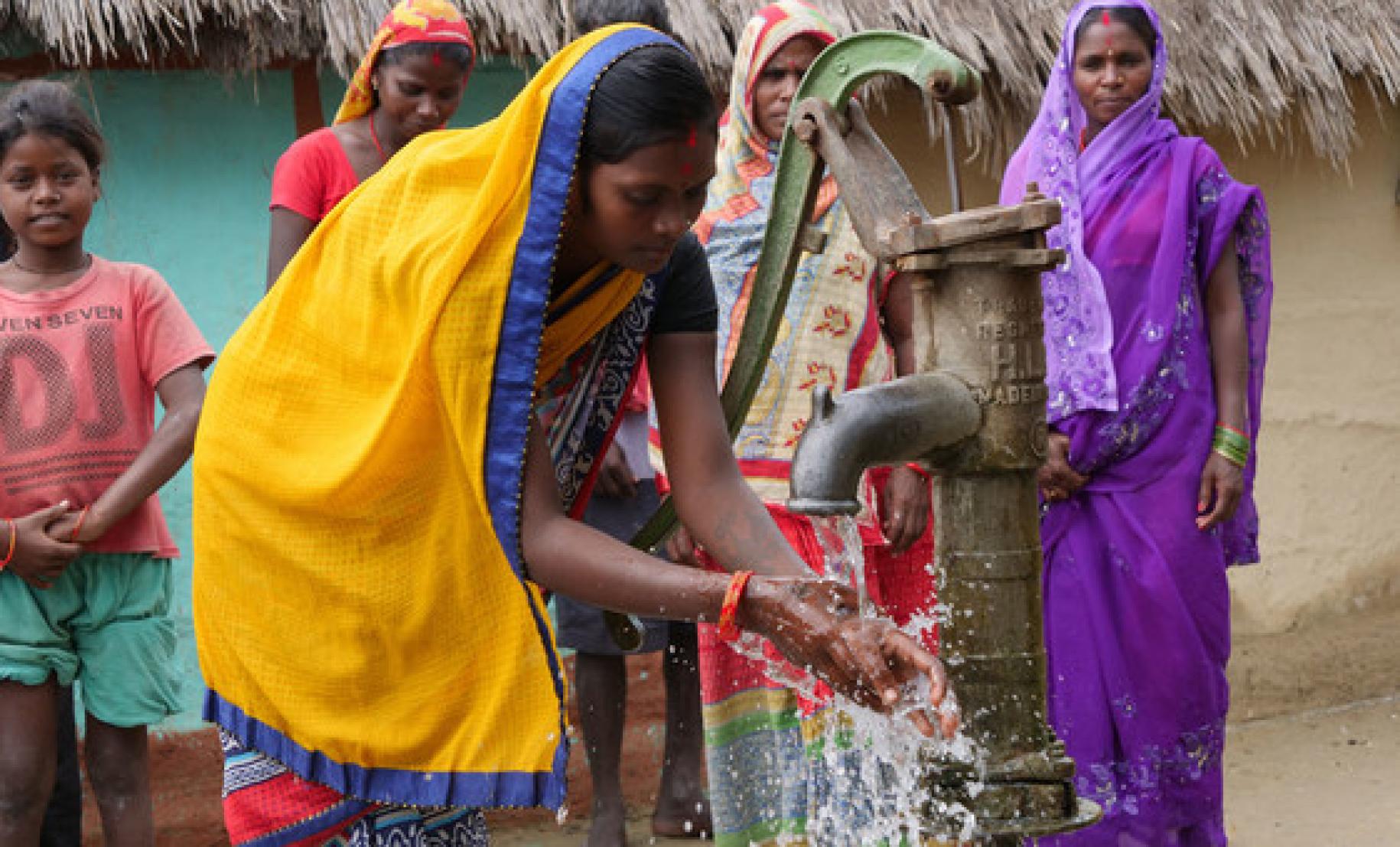The embed image shows women and girls at a water pump washing their hands. 