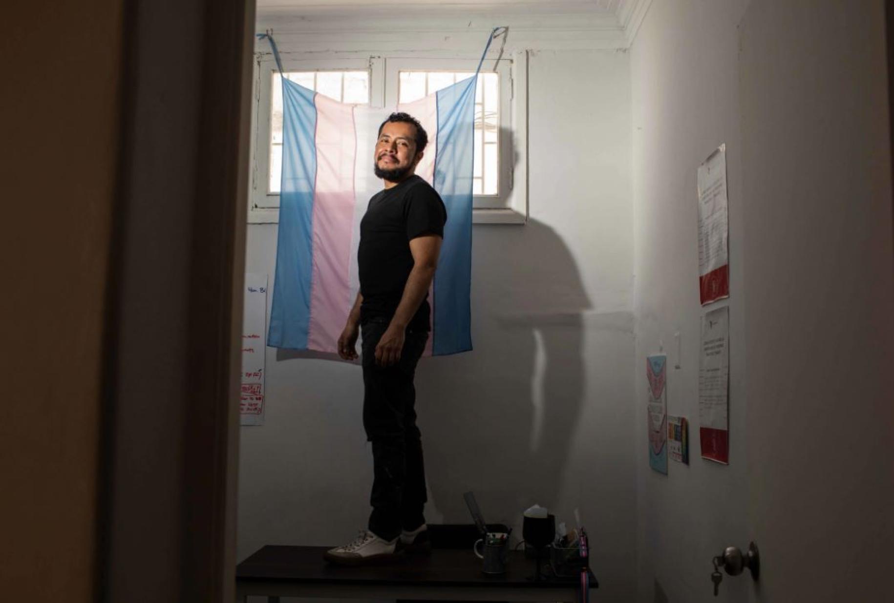 Photo shows Marco standing atop a desk, as he stands in front of a flag draped over a window.