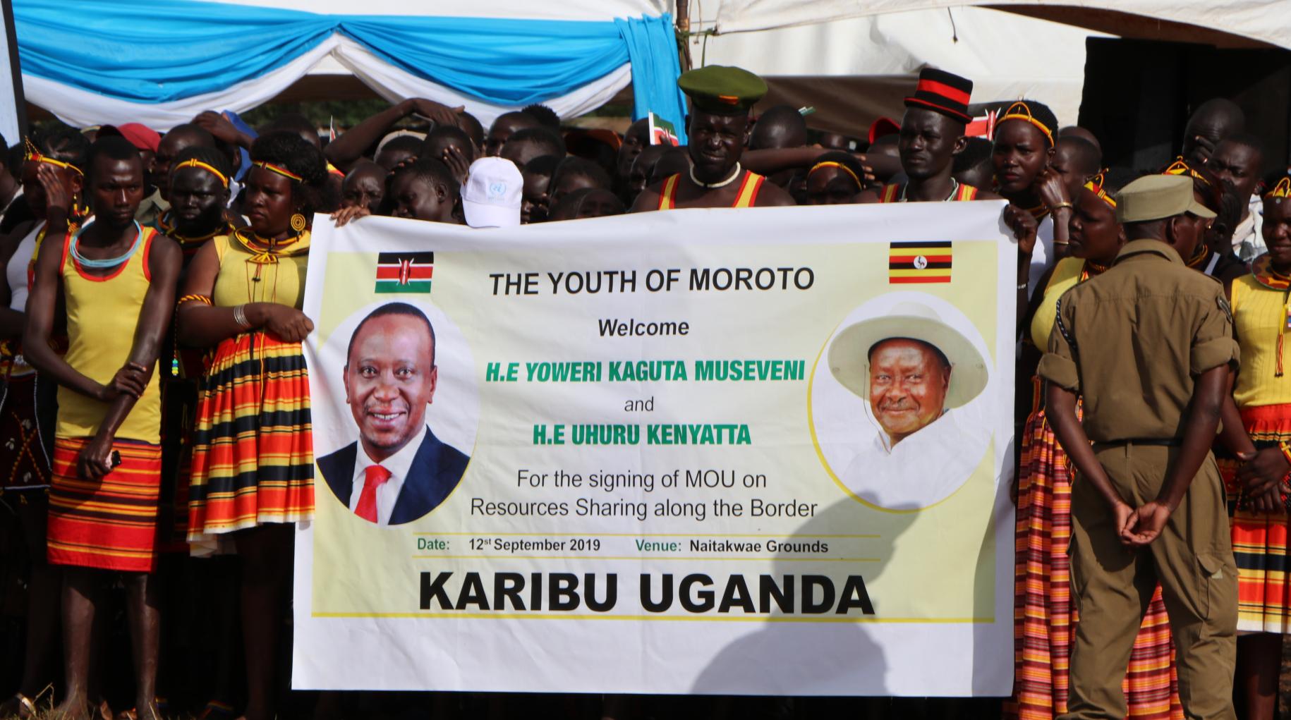 Shows a group of people holding a banner that shows heads of Kenya and Uganda.
