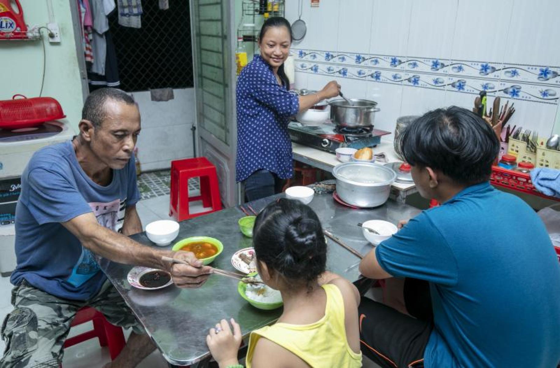 Shows Shows the family in the kitchen. Chau Bao, Ben Tre cooks dinner, while looking happily at her family sitting at the dinner table eating.