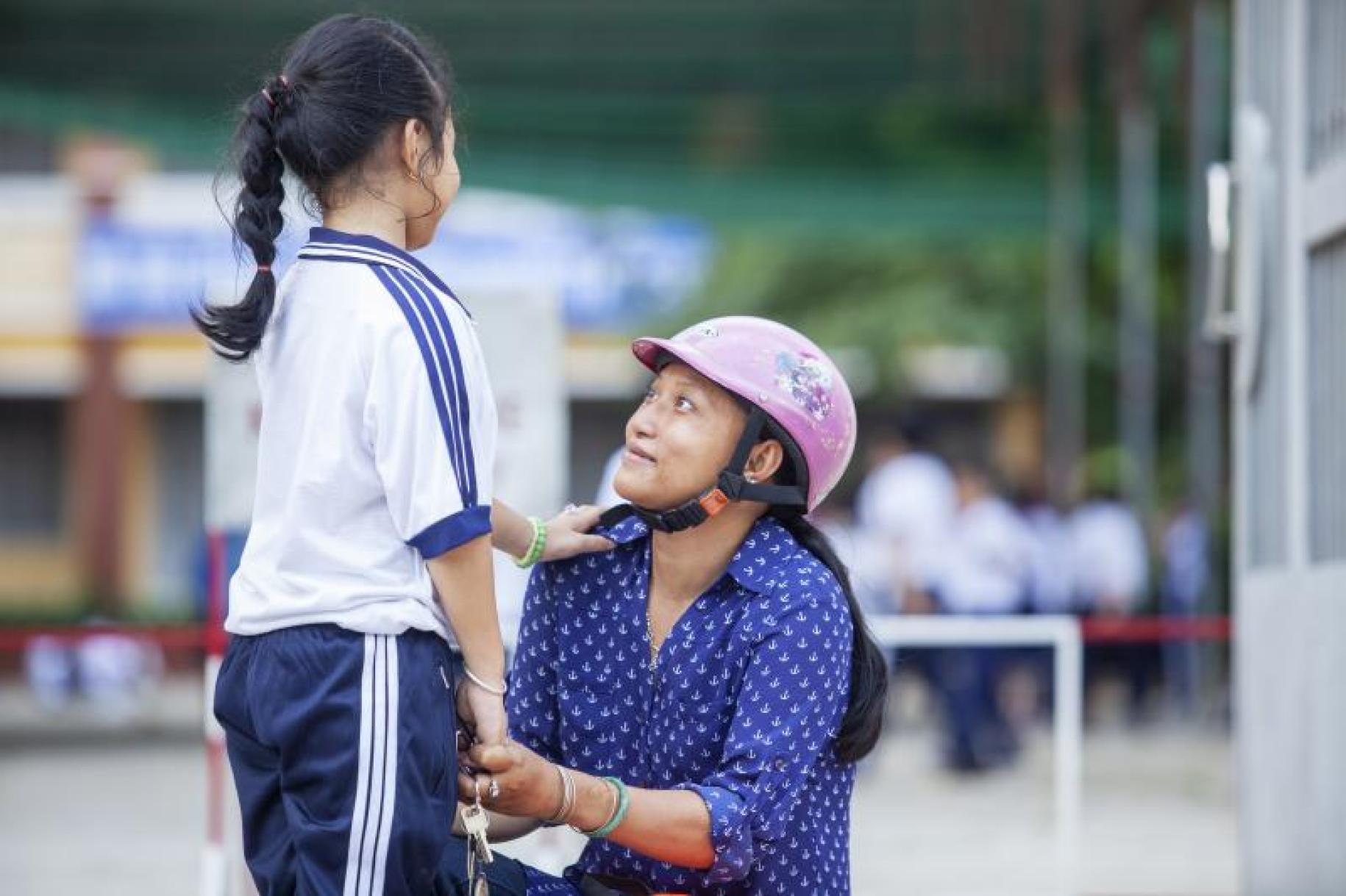 Chau Bao, Ben Tre wearing a helmet, kneels as she lovingly gazes at her daughter, who is standing facing her with one hand on her mother's shoulder.