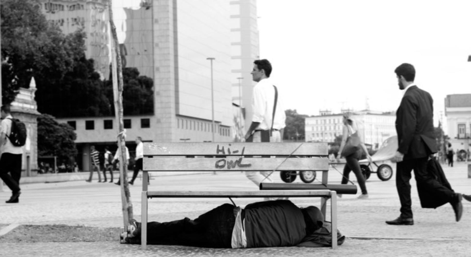 A homeless person sleeps in the streets under a bench in Rio.