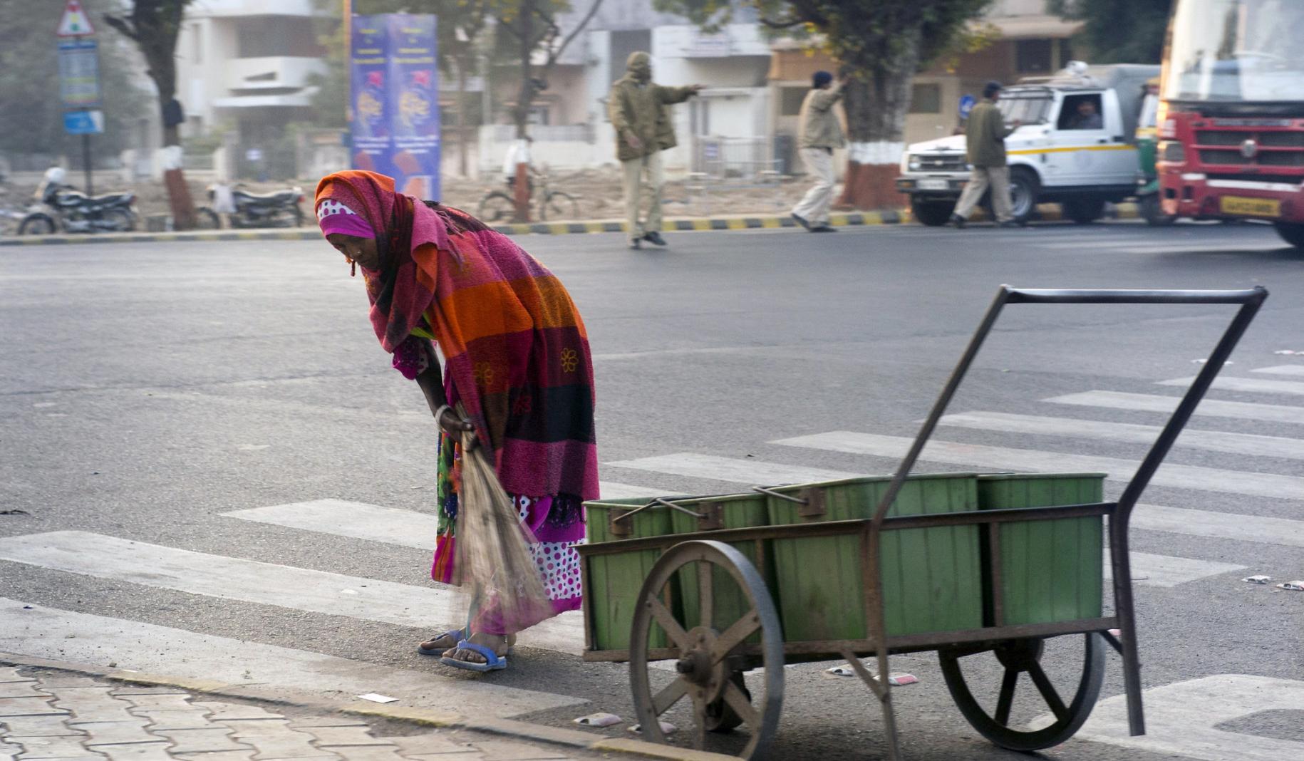 Woman is shown sweeping the street near a cart on the road.