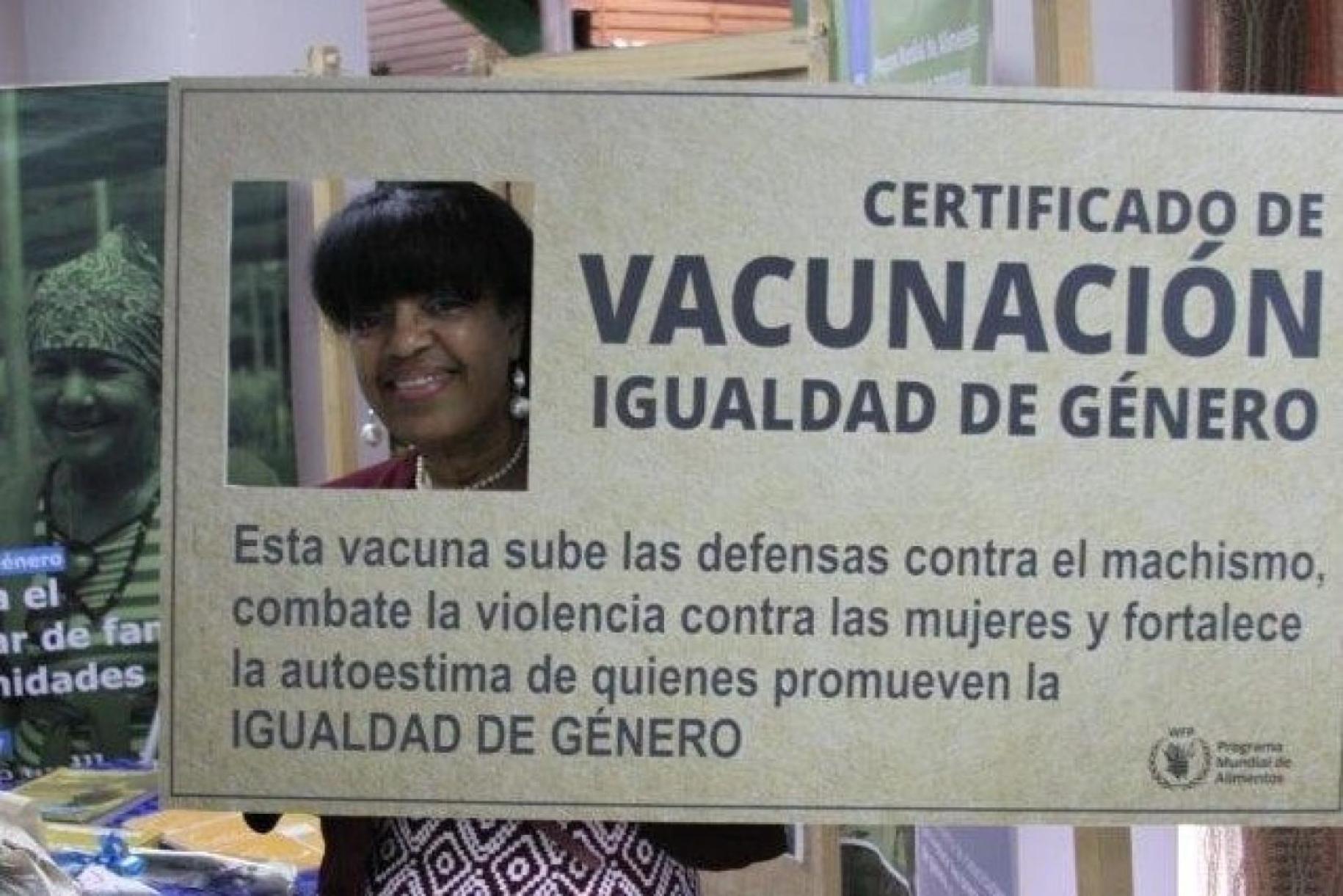 Yudith stands with her head in a cut of a giant-sized gender equality certificate.
