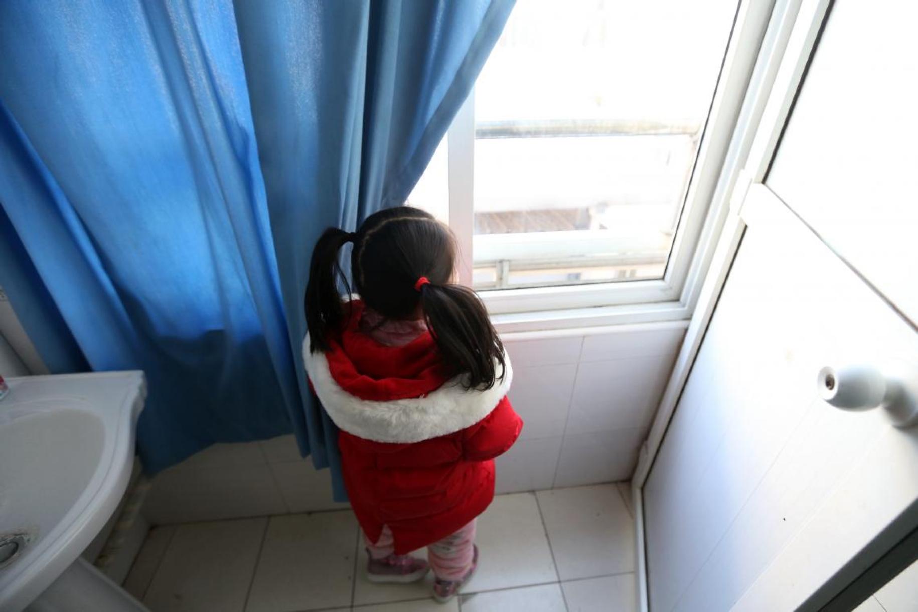 فتاة صغيرة تنظر من النافذة.