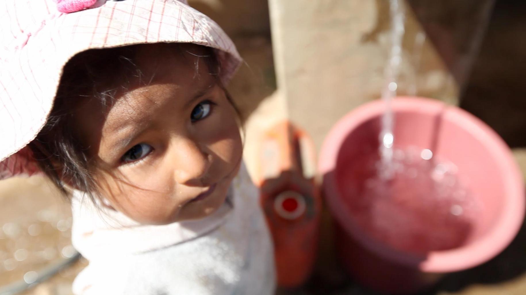 Little girl looks at the camera as water fills her container.