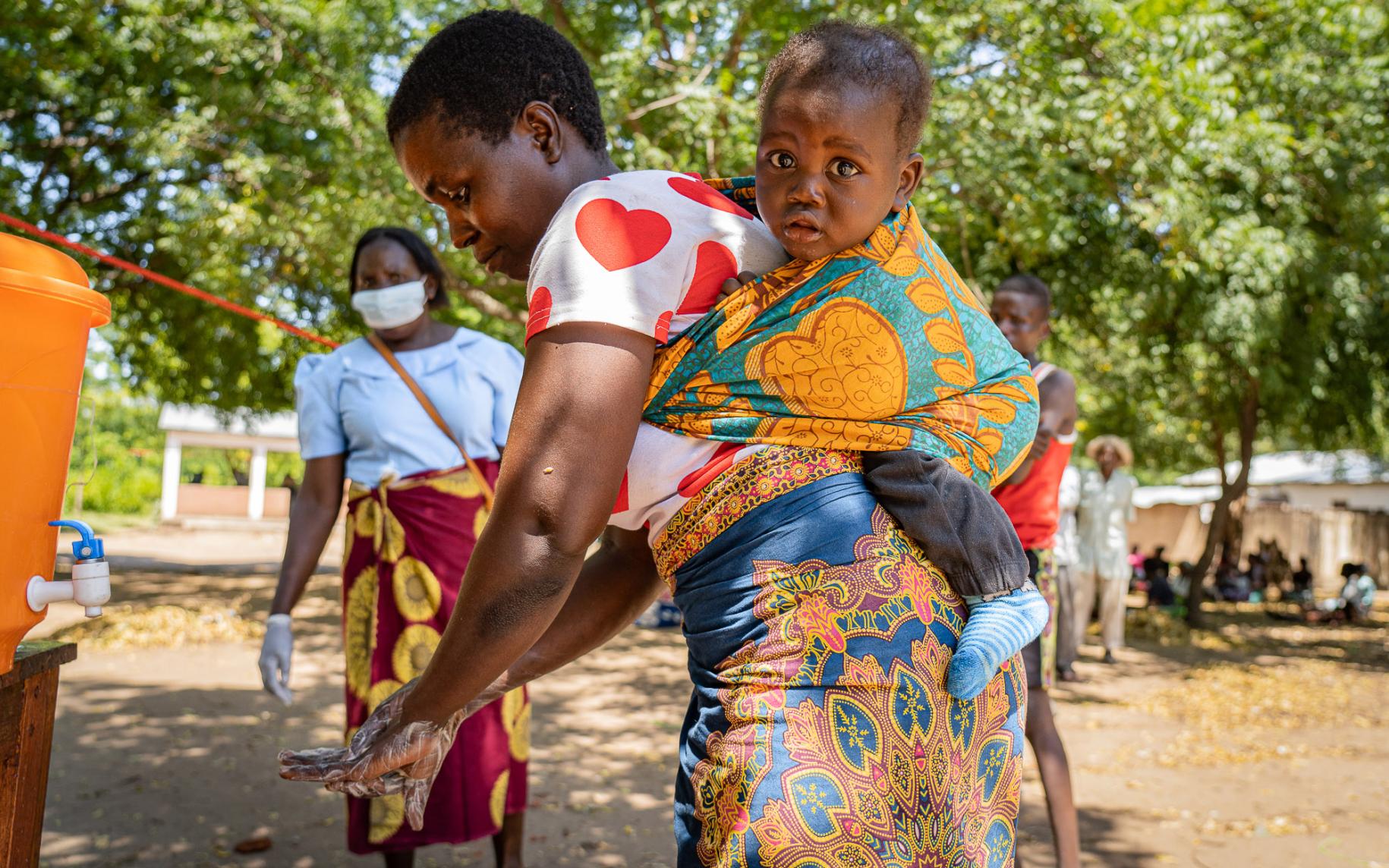 تظهر أليناف نهلاني، وهي مزارعة الكفاف، تغسل يديها وتحمل طفلها على ظهرها.