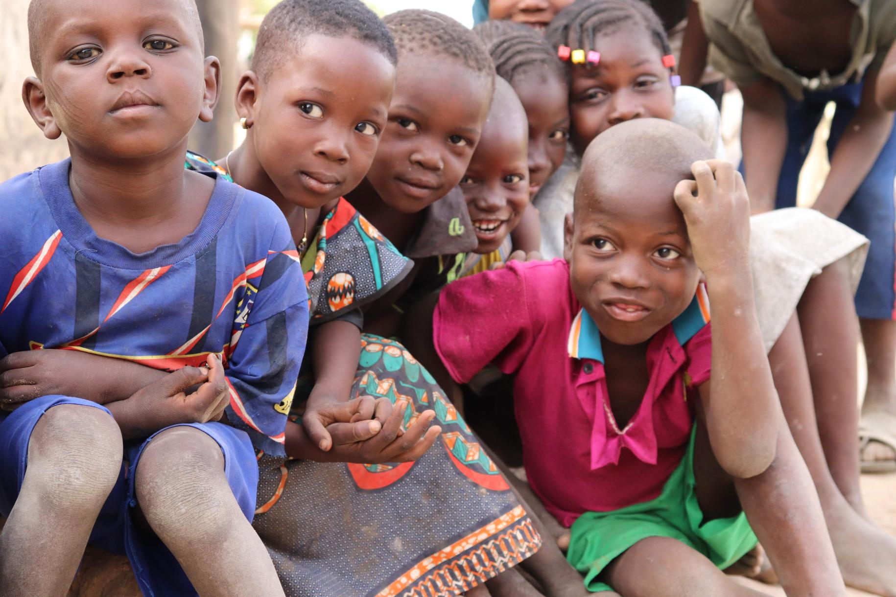 Young children sit together and look curiously at the camera. Birth certificates help ensure these and other children are not left behind.