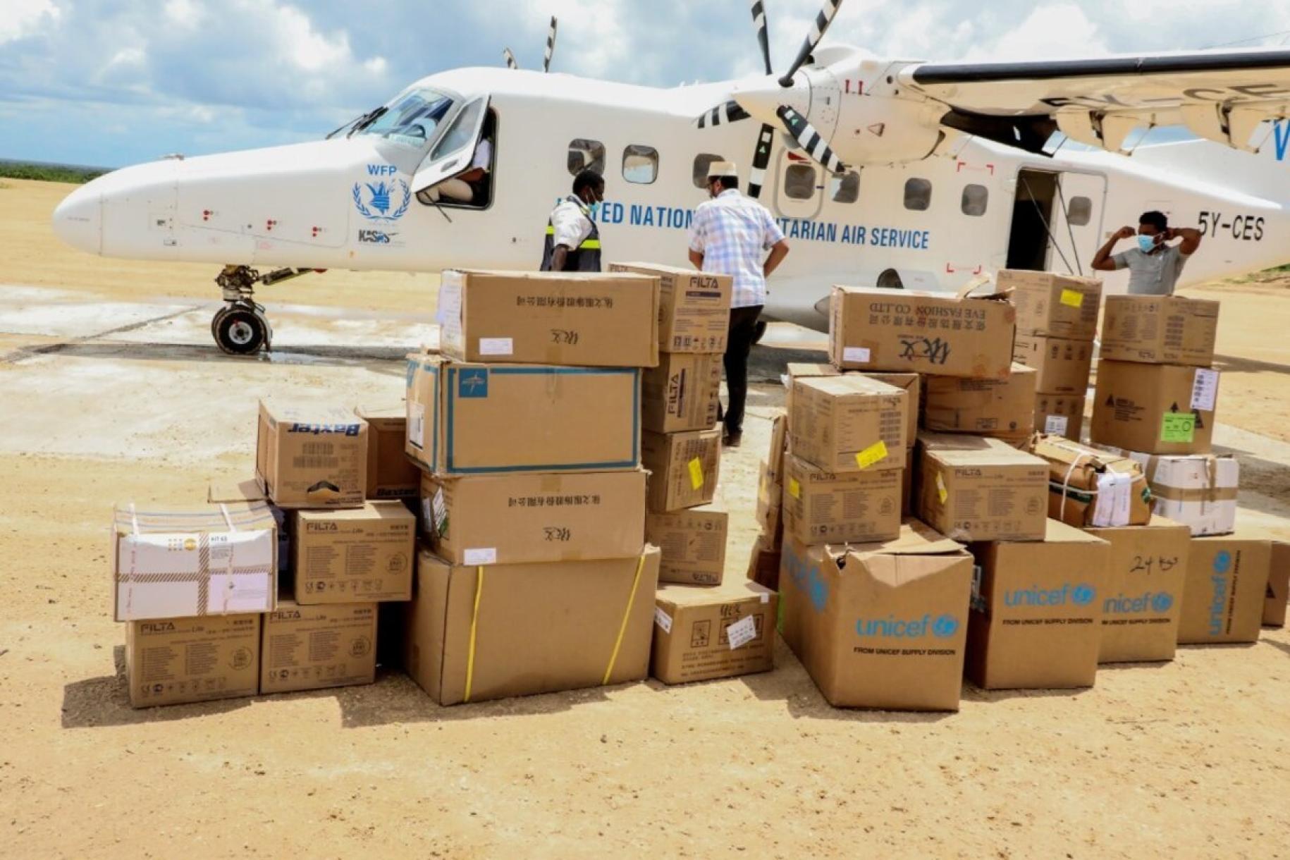An aircraft with the WFP emblem is shown with boxes of supplies in the foreground.