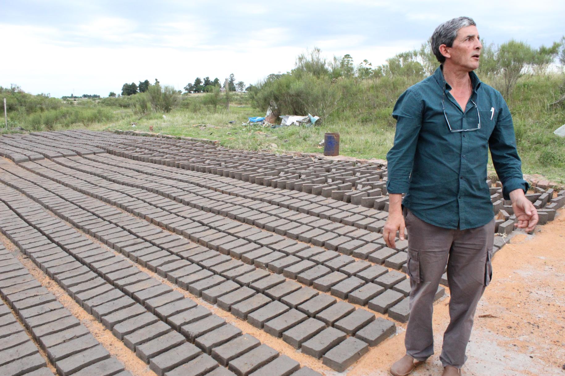Eduard Romero stands in front of the bricks spread across the ground set under the sun to dry.