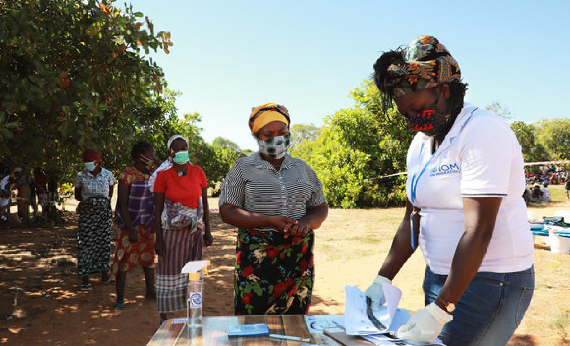 Dans la province de Cabo Delgado, un membre féminin du personnel de l'OIM procède à l'accueil de femmes déplacées, qui font la queue en attendant d'être enregistrées. Toutes les femmes portent un masque de protection respiratoire.