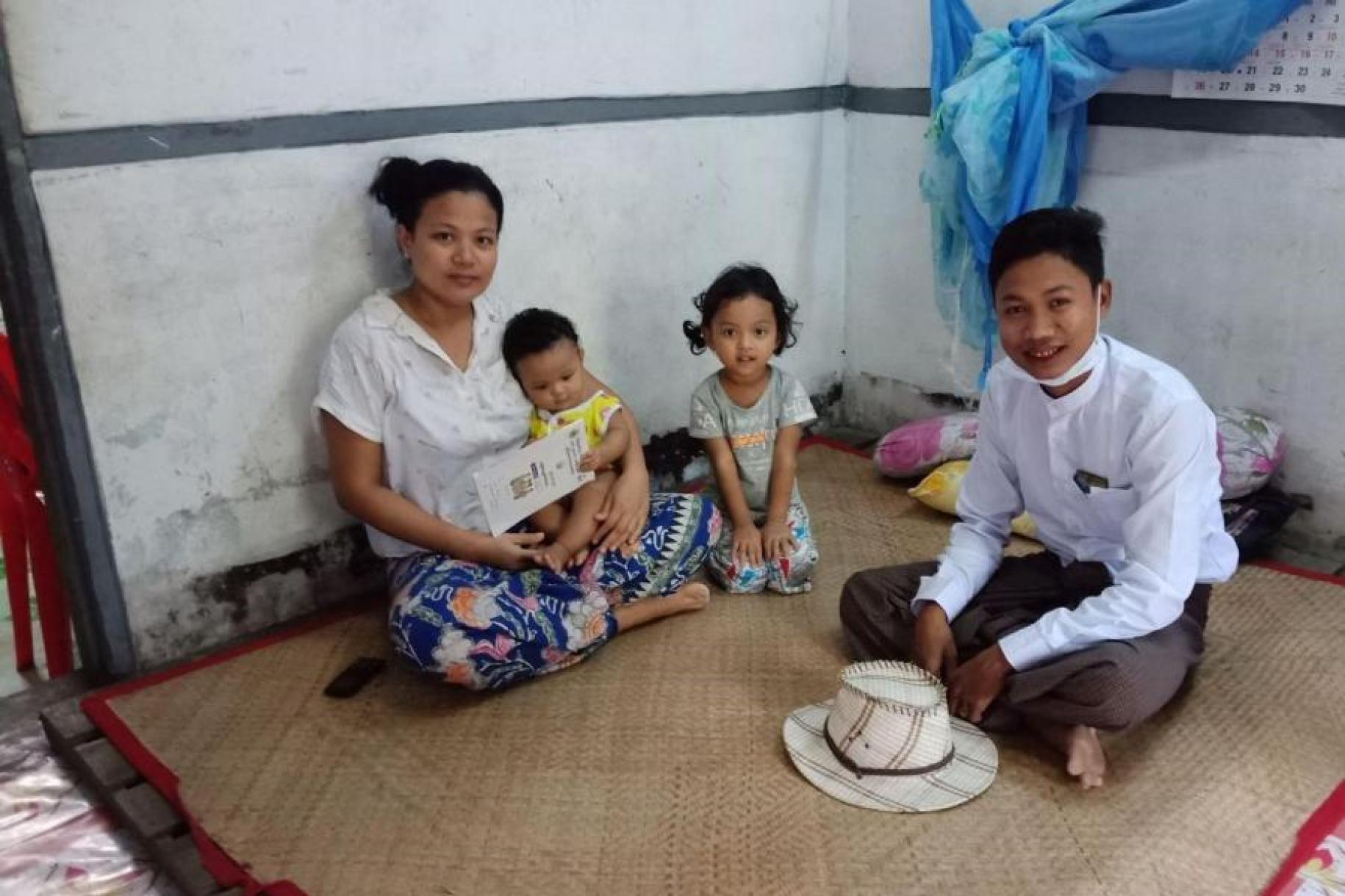 A woman sits with her children and husband on the floor of their residence.