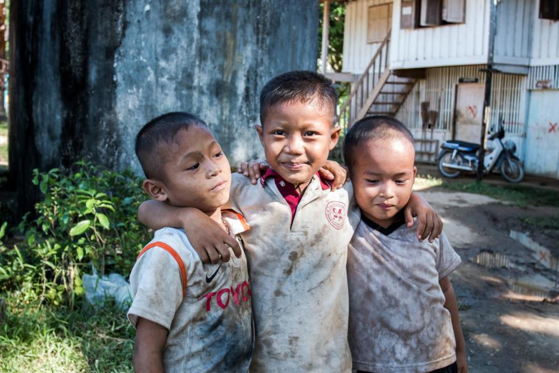Three young boys with their arms across each other pose for the camera. 