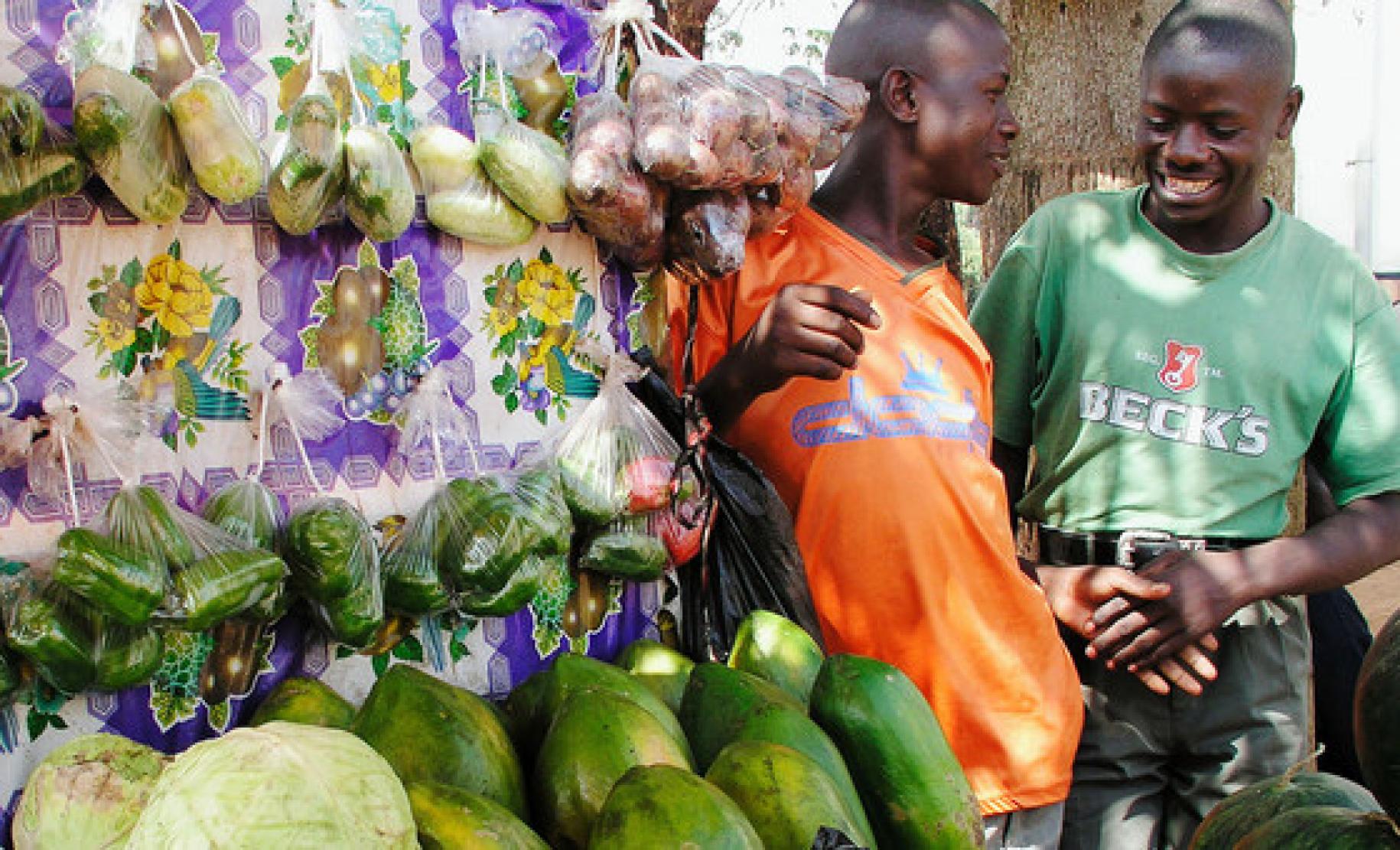 Two market vendors chat by a vegetable stand in a marketplace in Kampala, Uganda.