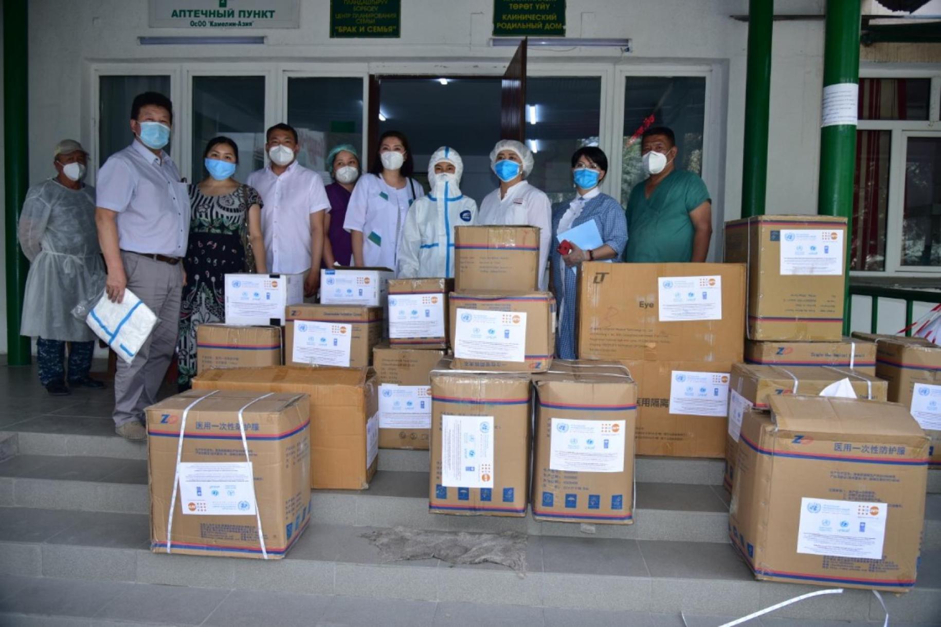 UN personnel and healthcare workers stand behind donation boxes wearing protective gear.