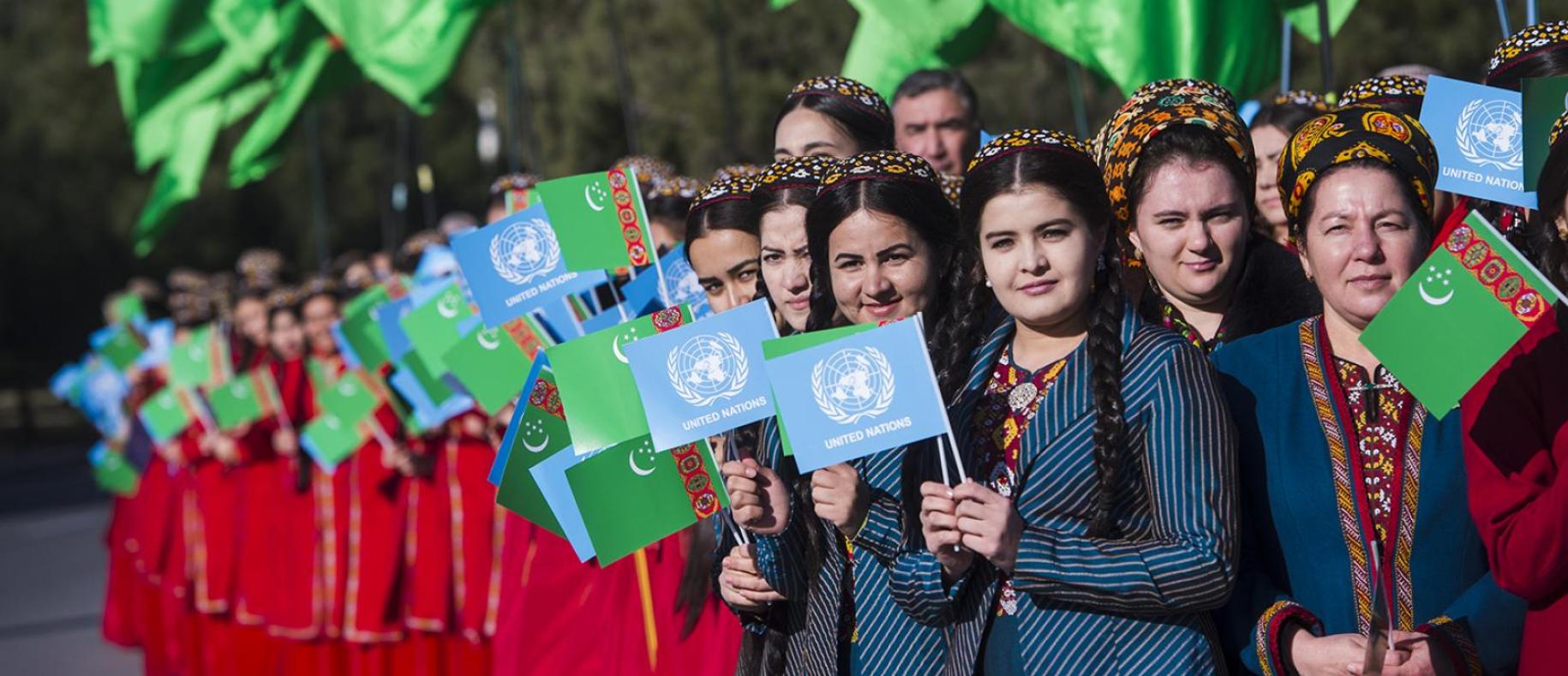 شابات يحملن علم الأمم المتحدة وتركمانستان أثناء احتفالهن بافتتاح دار الأمم المتحدة.