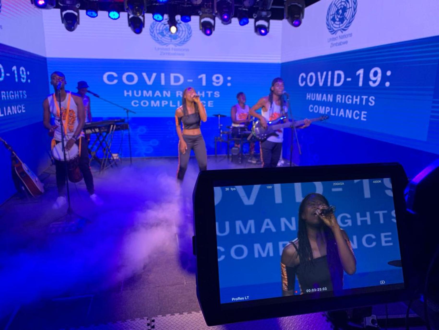 Caroleen Masawi and her band perform surrounded by green screens featuring a COVID-19 message.