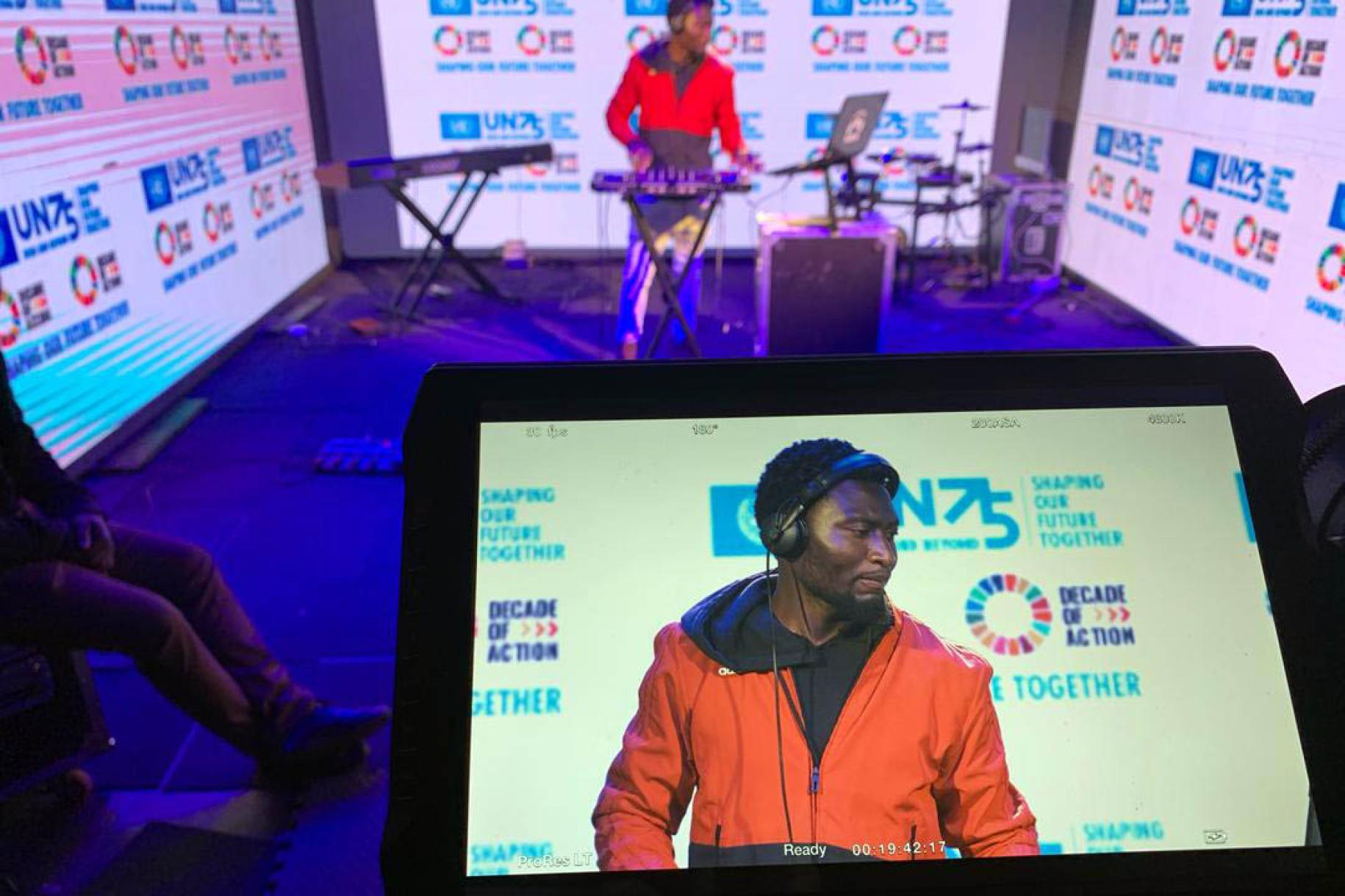 DJ Yayos performs while being recorded. The photo shows him in the background with an image of him on an screen in the foreground.
