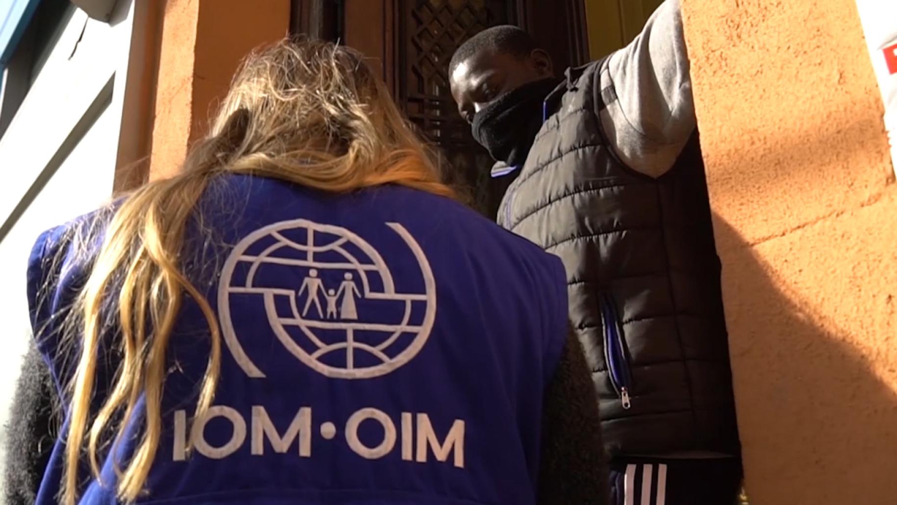 Un miembro del personal de la OIM habla con un hombre a la entrada de su casa.