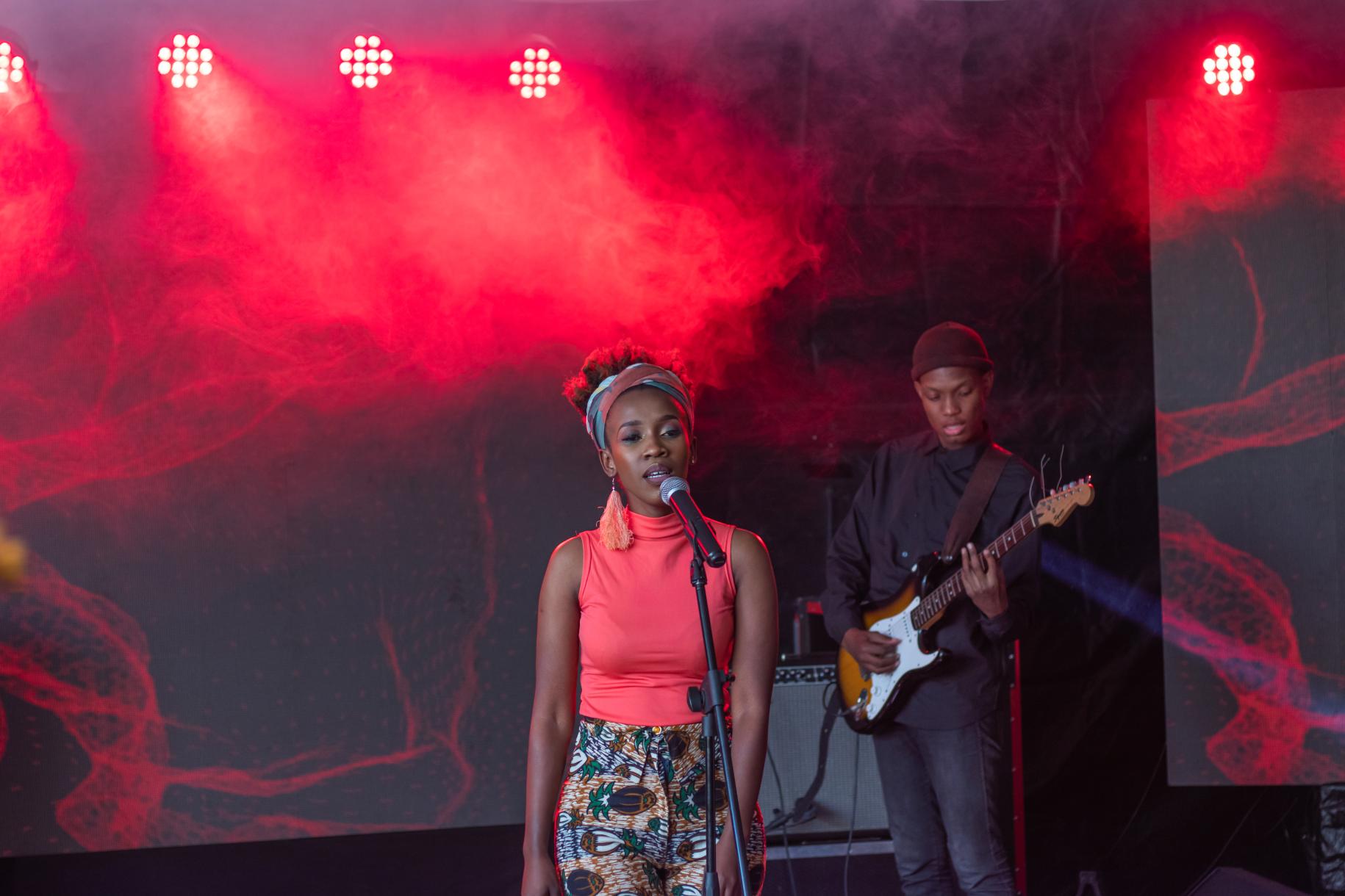 Musician Vuyo Brown sings at a microphone, while her bassist plays in the background. 