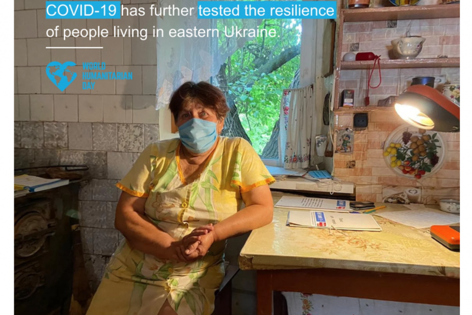 A woman wearing a face mask leans on her desk with a factoid above stating COVID-19 has tested the resilience of people living in eastern Ukraine.